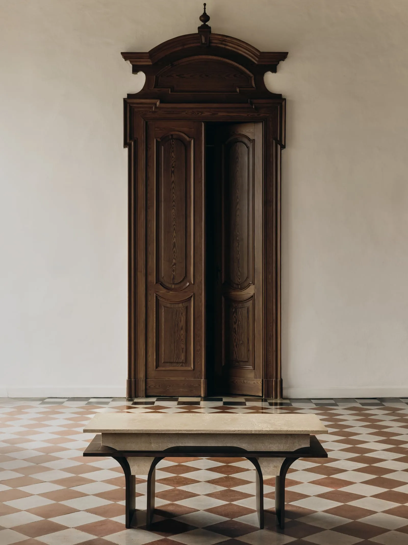 Arcus Bench in front of a tall carved wooden door, on a terracotta and white checked floor