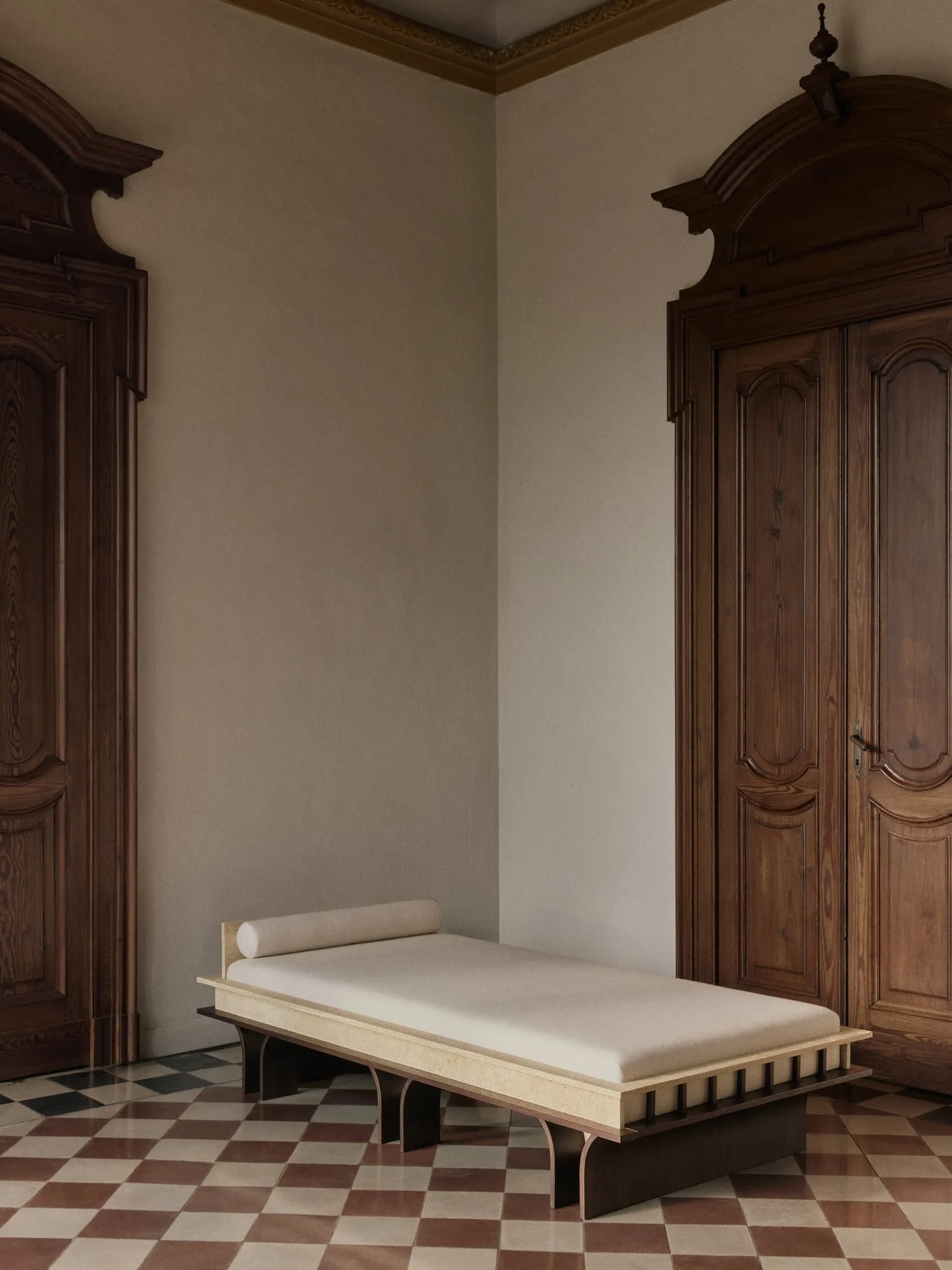 Arcus Daybed from a three-quarter angle between two carved wooden doors