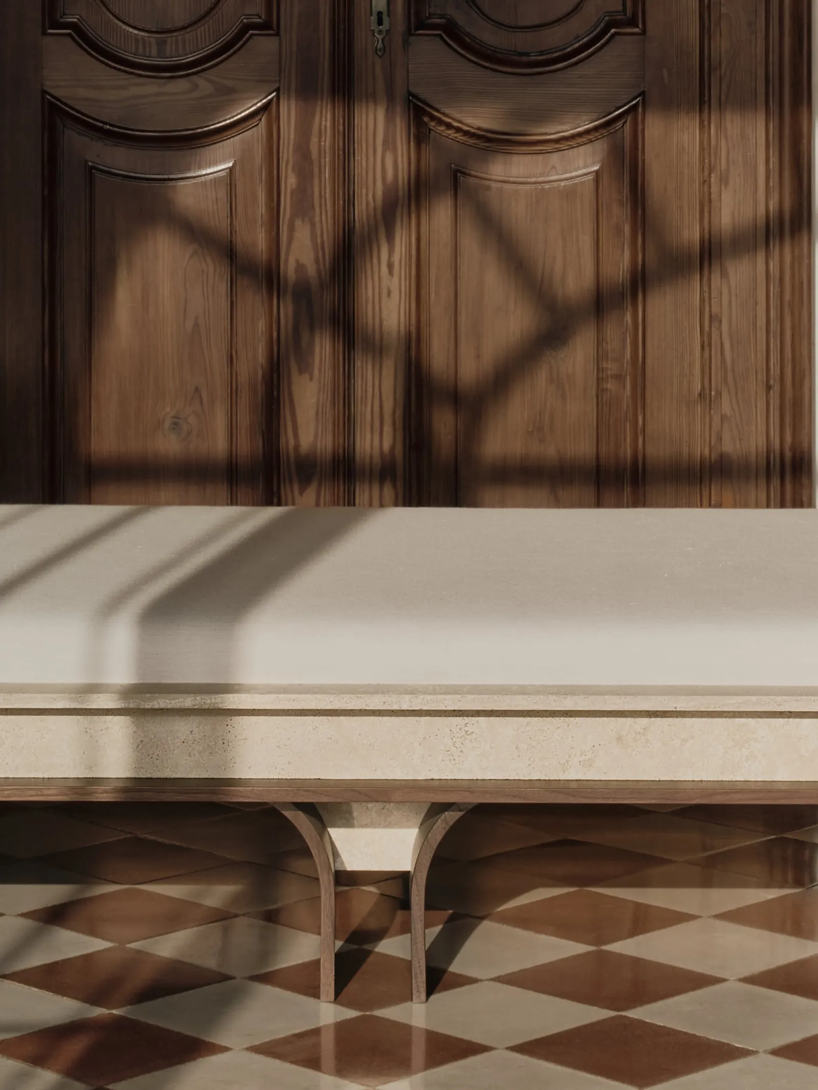 Close view of the Arcus Daybed travertine frame and cushion, with the shadow of a window across the door behind