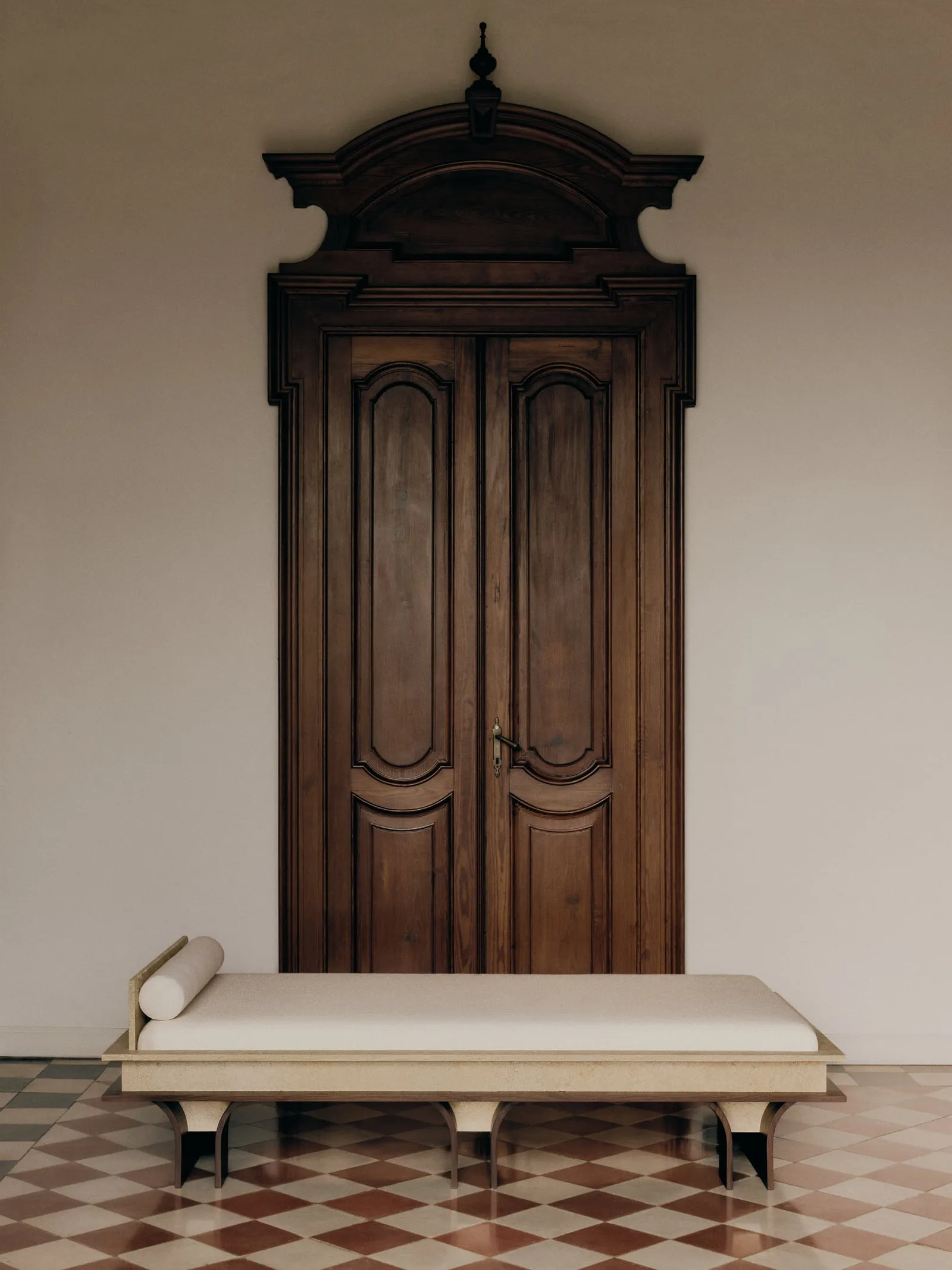 Arcus Daybed in front of a tall carved wooden door, on a terracotta and white checked floor