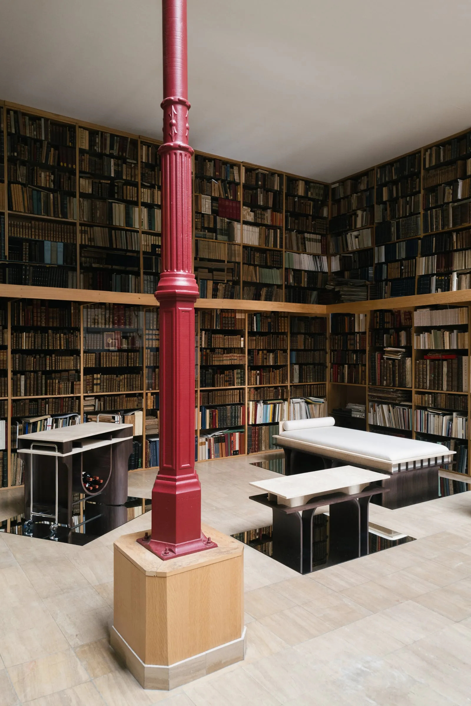 Arcus daybed, bench and bar cart among bookshelves in a bookshop, beside a red cast-iron column