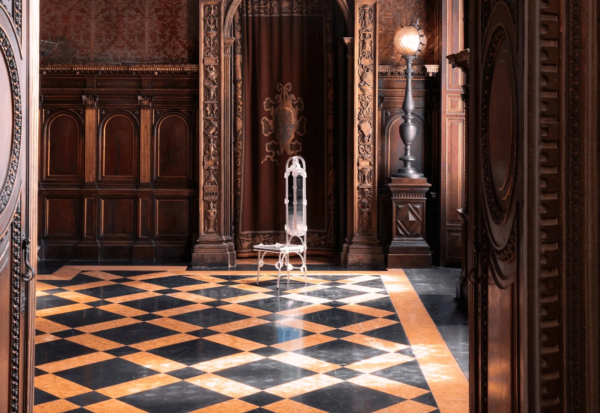 A Stemma glass chair in a carved wood-panelled hall with a chequered marble floor