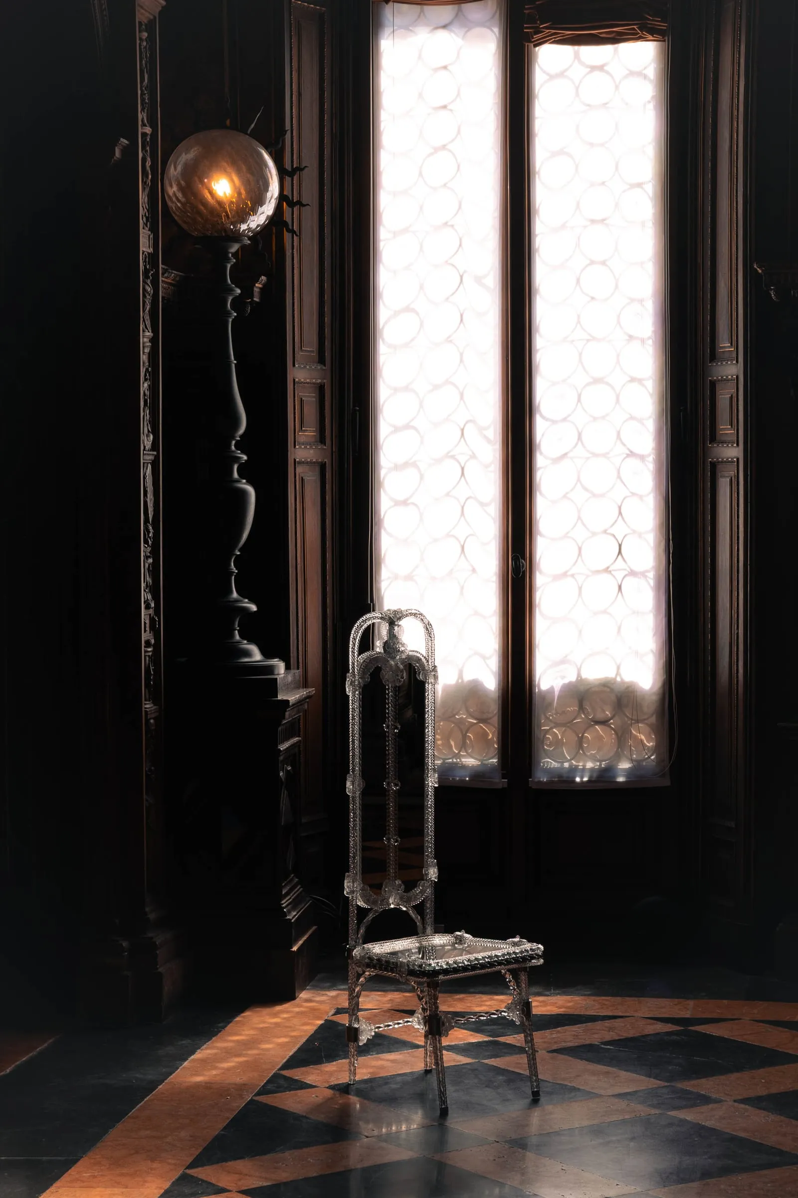 Stemma chair in Murano glass beside a tall window in a dark room
