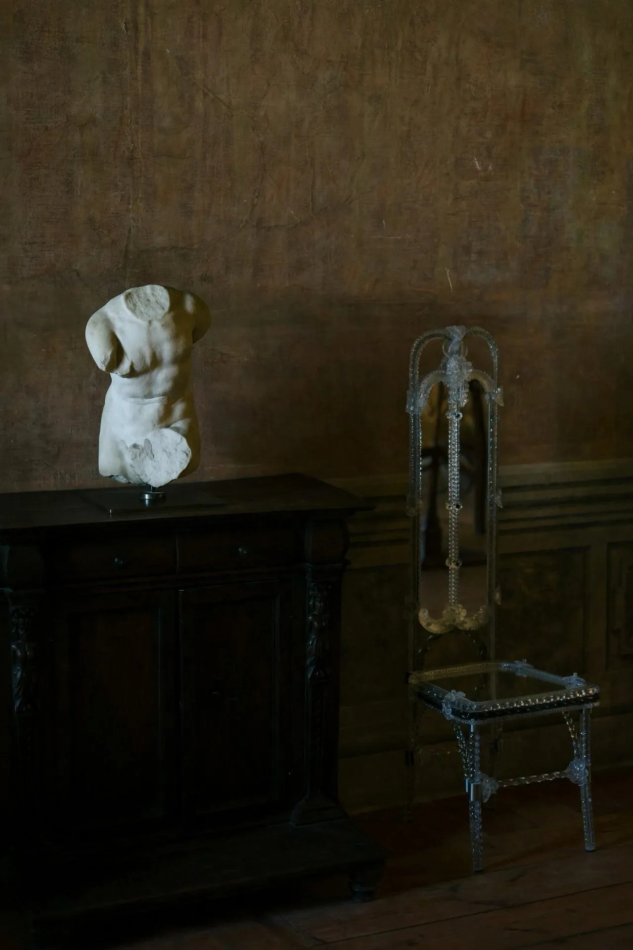 Stemma Dining Chair beside a classical marble torso on a dark wooden cabinet