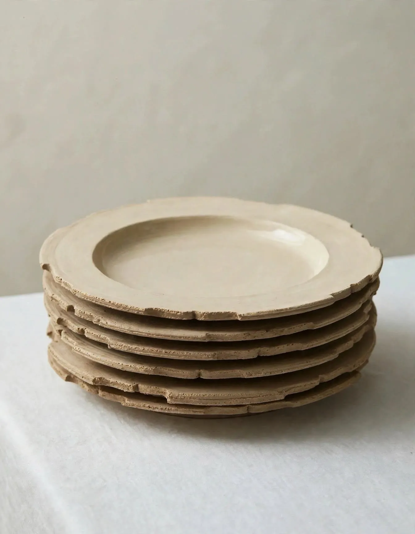 A stack of hand-made stoneware plates with scalloped, raw-edged rims