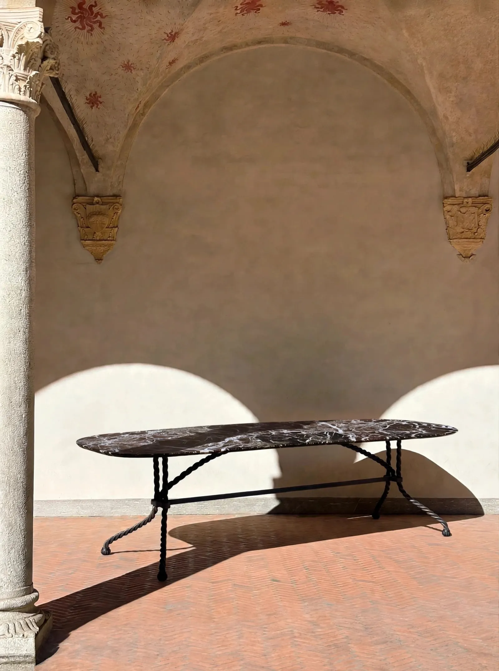 Tresse Brasserie Table with an oval marble top in a sunlit cloister