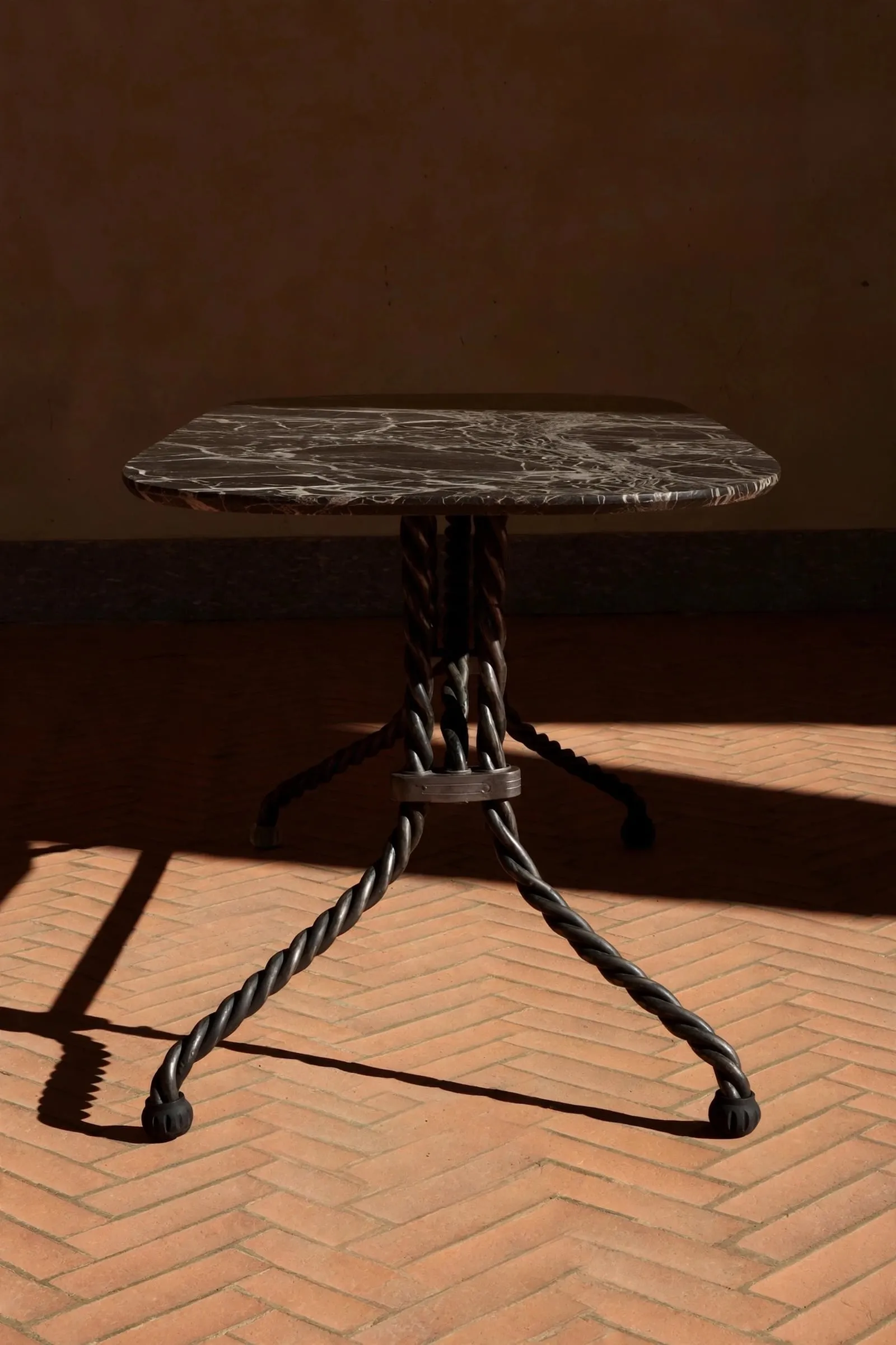 Tresse table with a marble top on a twisted metal base, on a brick floor