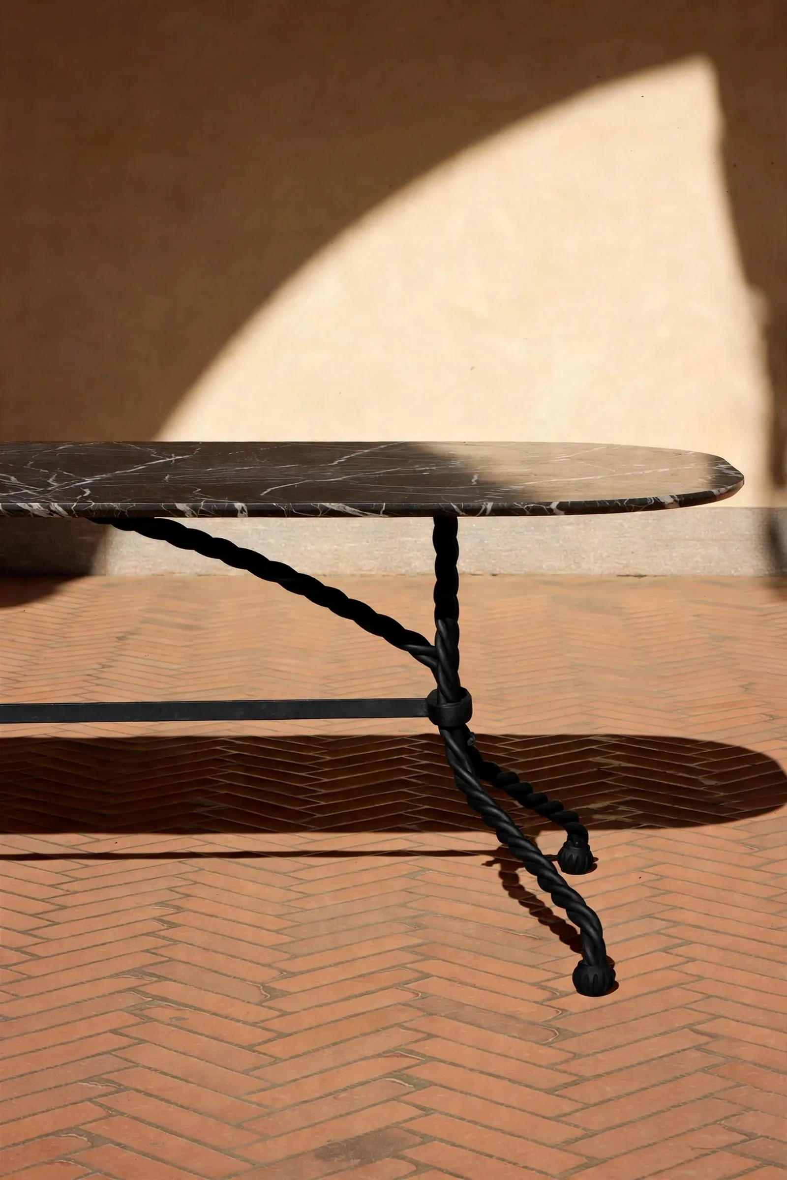 Tresse Brasserie Table in black marble on twisted metal legs, in sunlight
