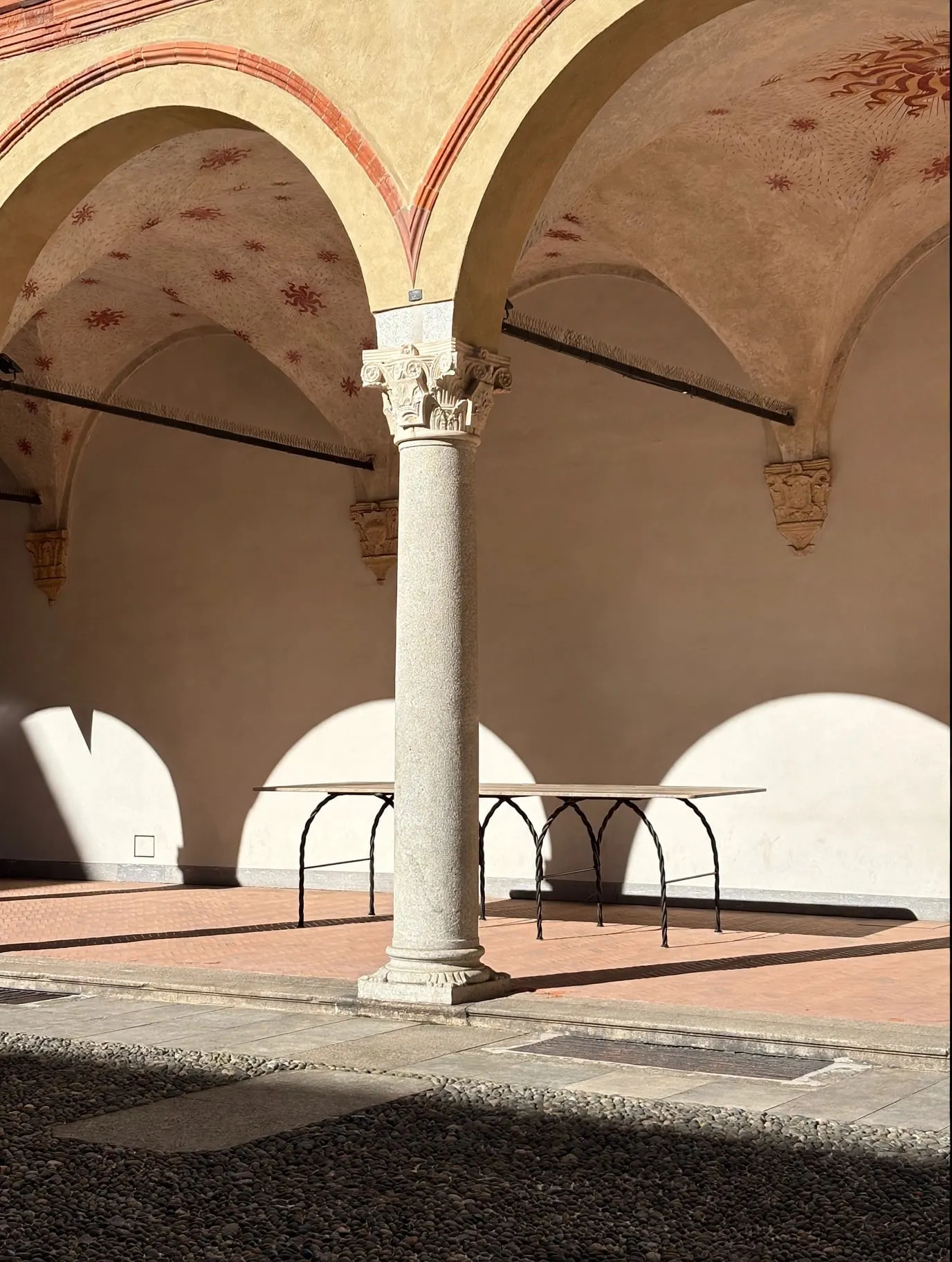 Tresse Città Table beneath the arches and columns of a frescoed courtyard