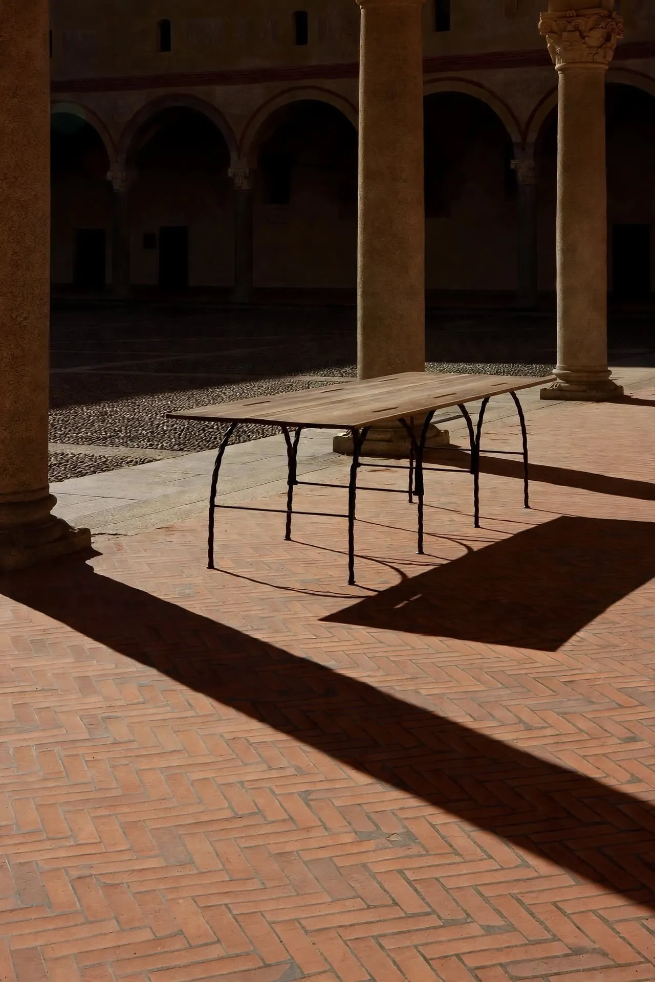 Tresse Città Table in a courtyard with long shadows on a herringbone brick floor