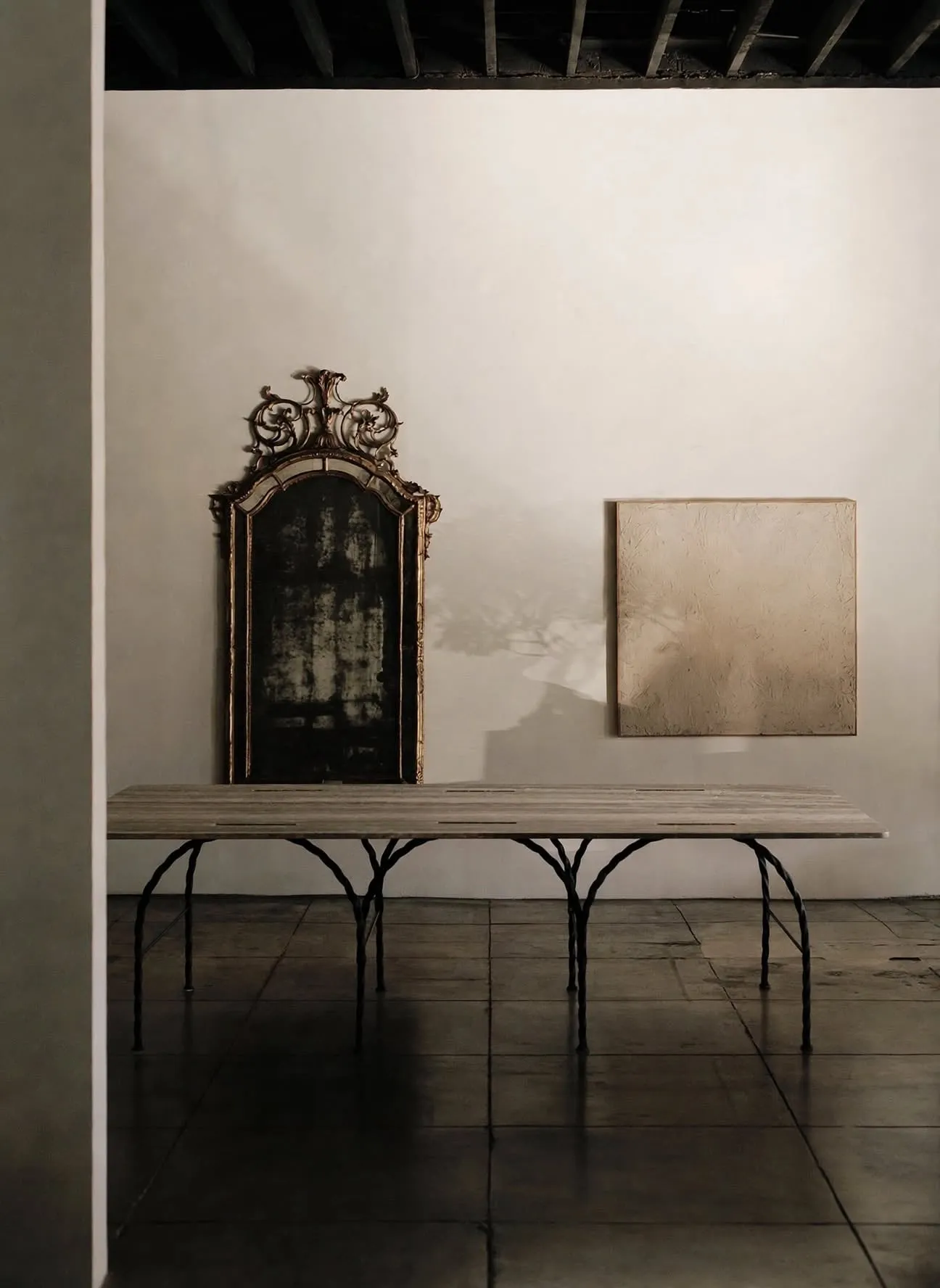 Tresse Città Table with braided arched legs in a room with weathered walls and a gilt mirror