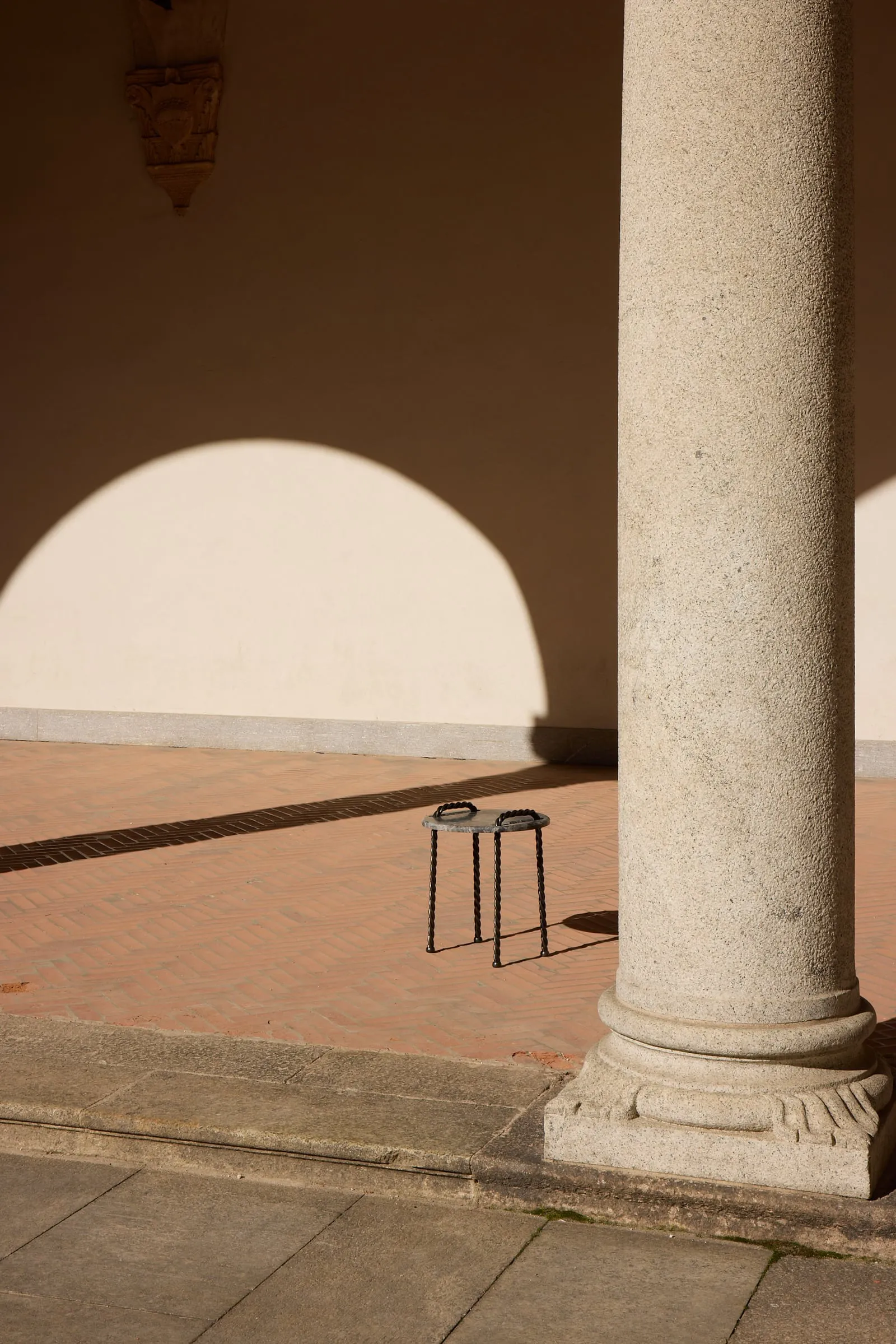 Tresse Side Table beside a stone column in a sunlit cloister