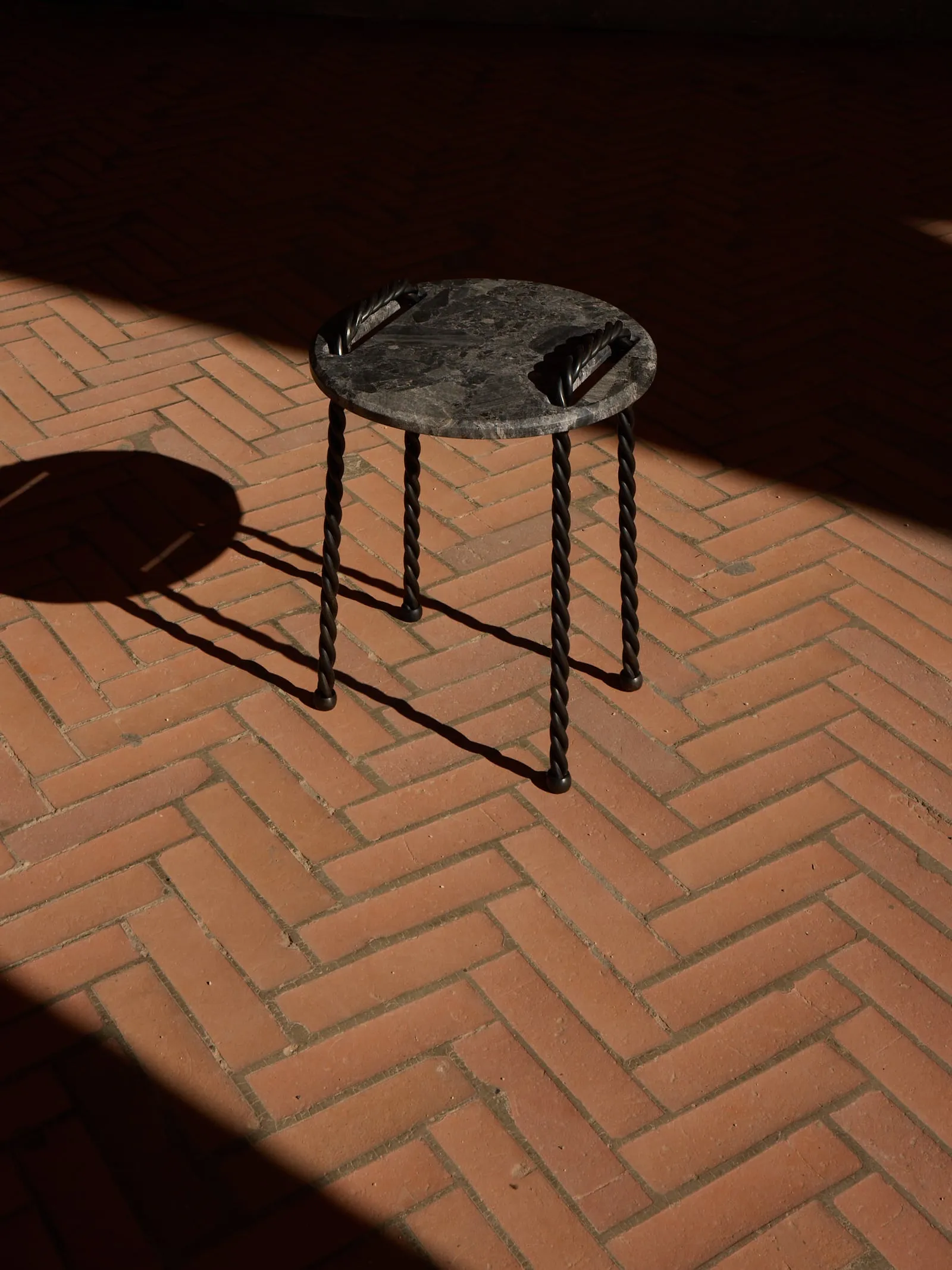 Tresse Side Table with a round black stone top on twisted metal legs