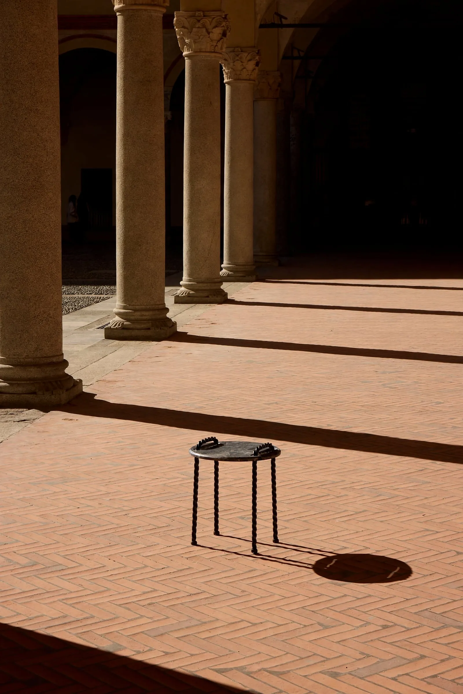 Tresse Side Table in a courtyard with long shadows across the brick floor